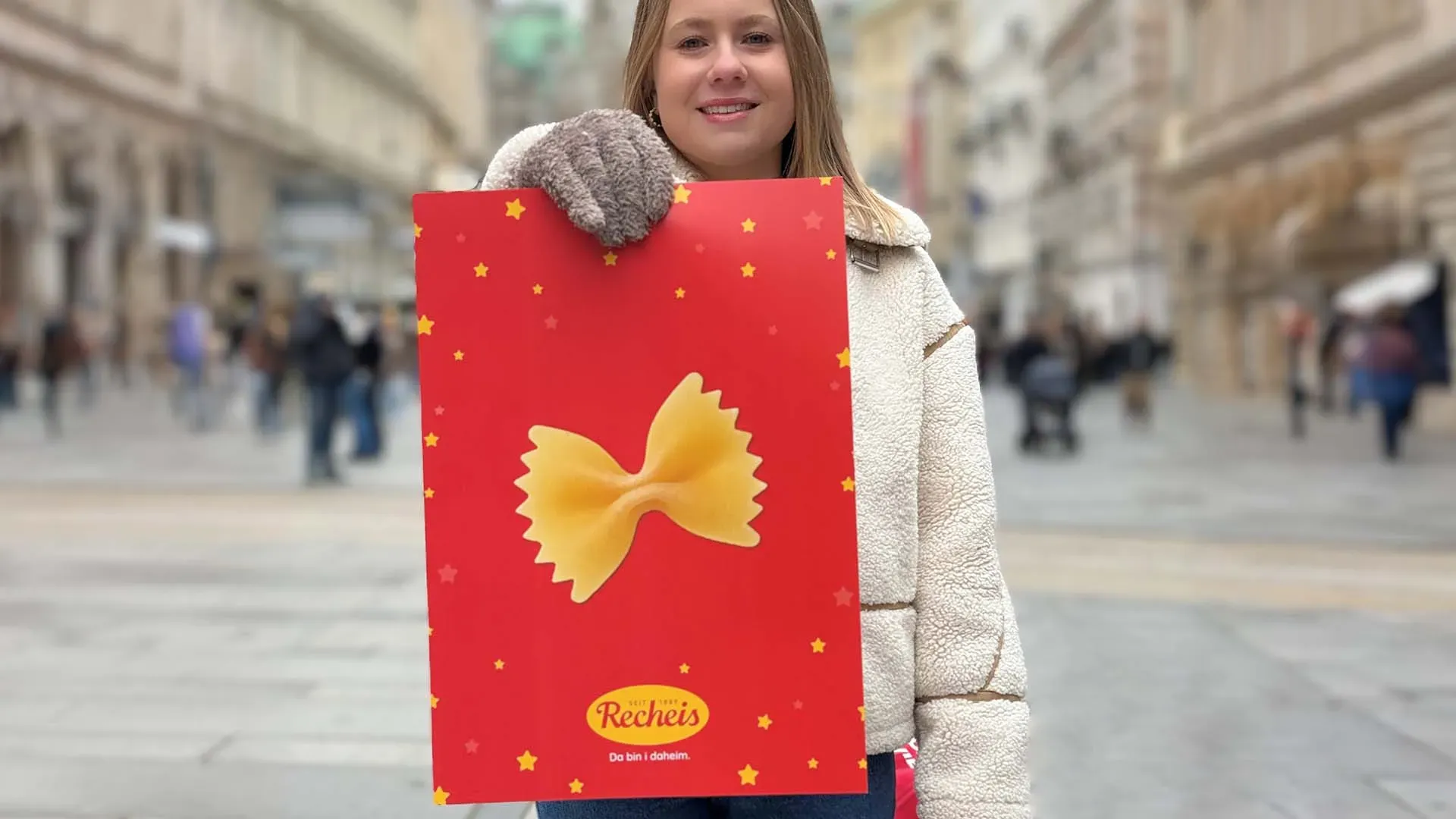 Lea bei der Straßenumfrage zum Weihnachtsrätsel 2025: Frau hält rote Tüte mit großer Farfalle auf belebter Straße
