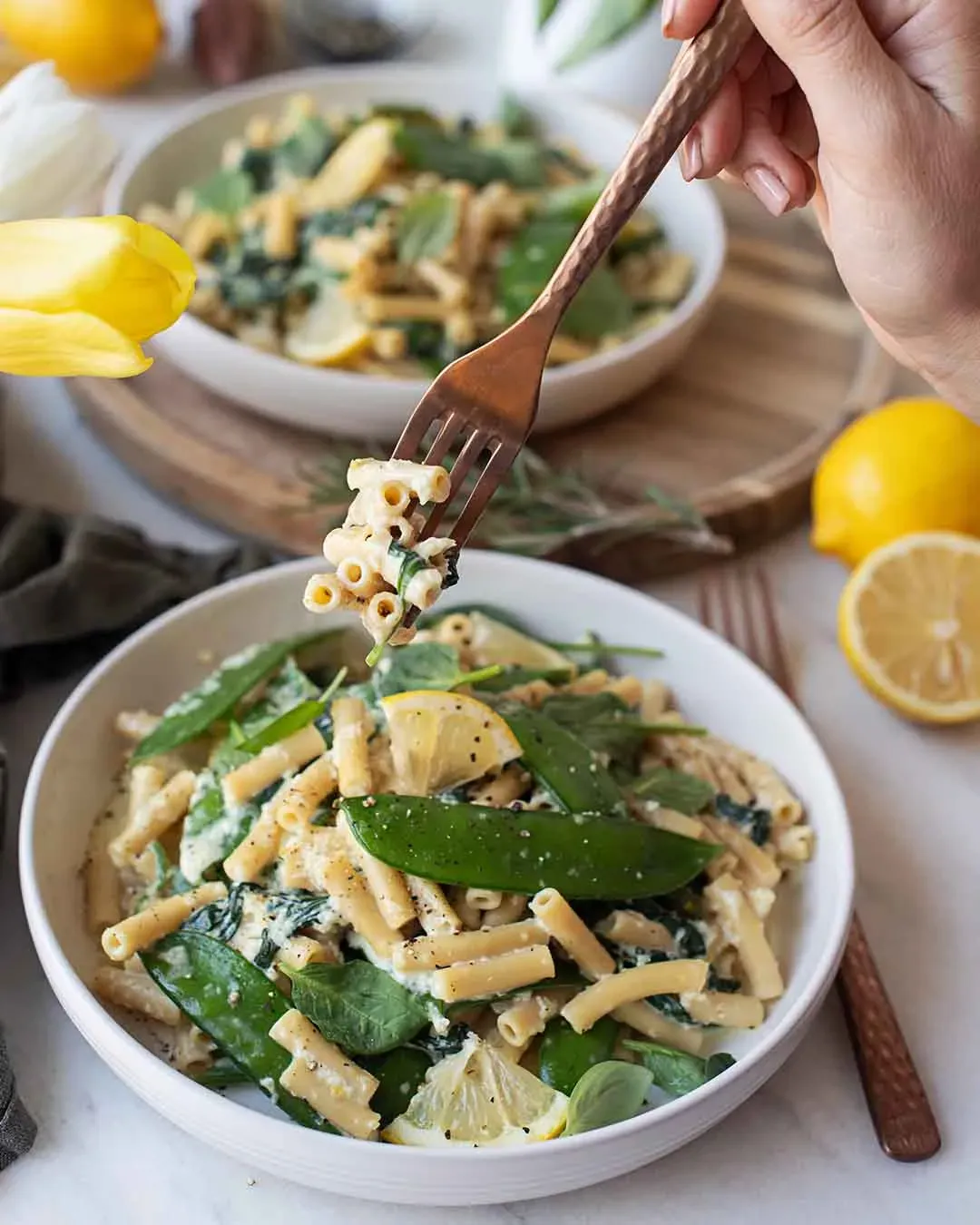 Lemon Pasta: Gabel mit Pasta und Gemüse über einer Schüssel mit Pasta, Zitrone und Erbsenschoten