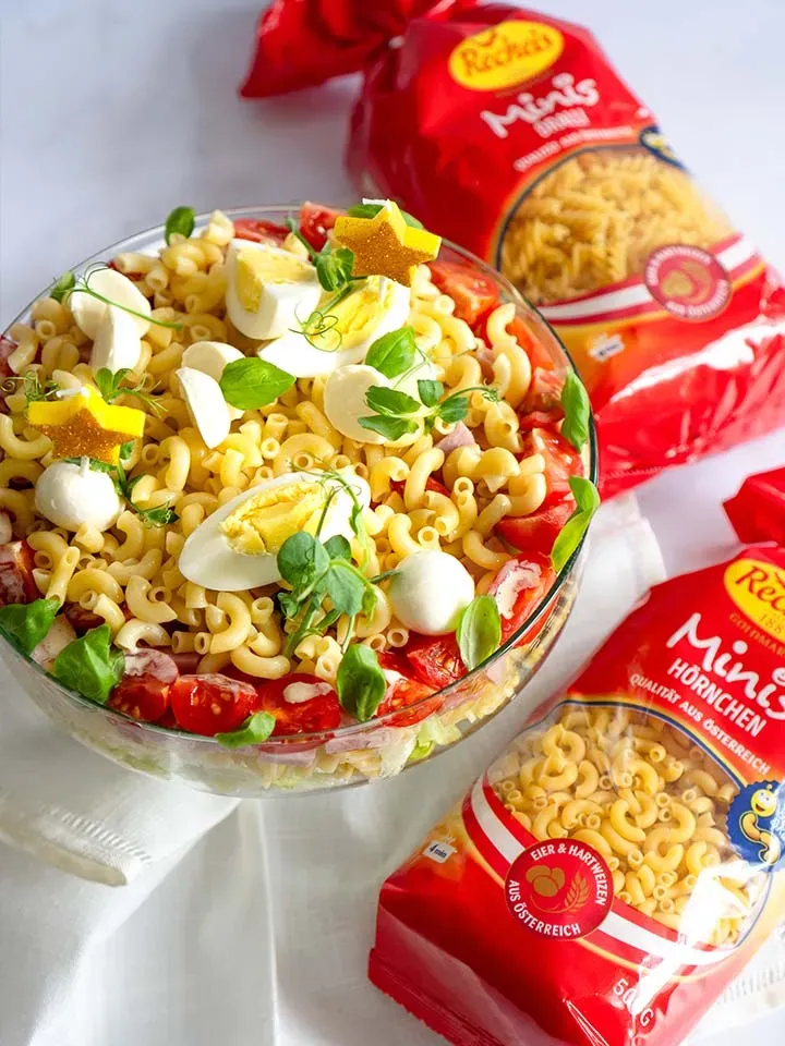 Nudelsalattorte mit Ei, Tomaten und Basilikum im Glas neben Nudelpackungen