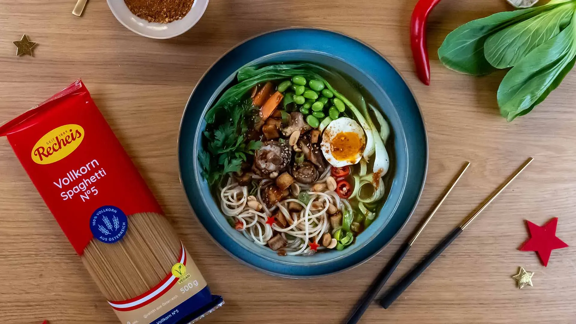 Bunte Schüssel vegetarische Ramen mit Nudeln, Gemüse und Ei neben einer Packung Vollkornspaghetti