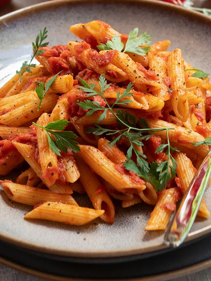 Salami-Dinkel-Penne in Tomatensauce, mit frischen Kräutern garniert, auf einem Teller