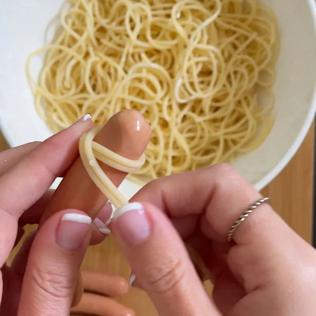 Hände wickeln Spaghetti um eine Wurst für Spaghetti-Mumien, davor eine Schüssel mit Spaghetti