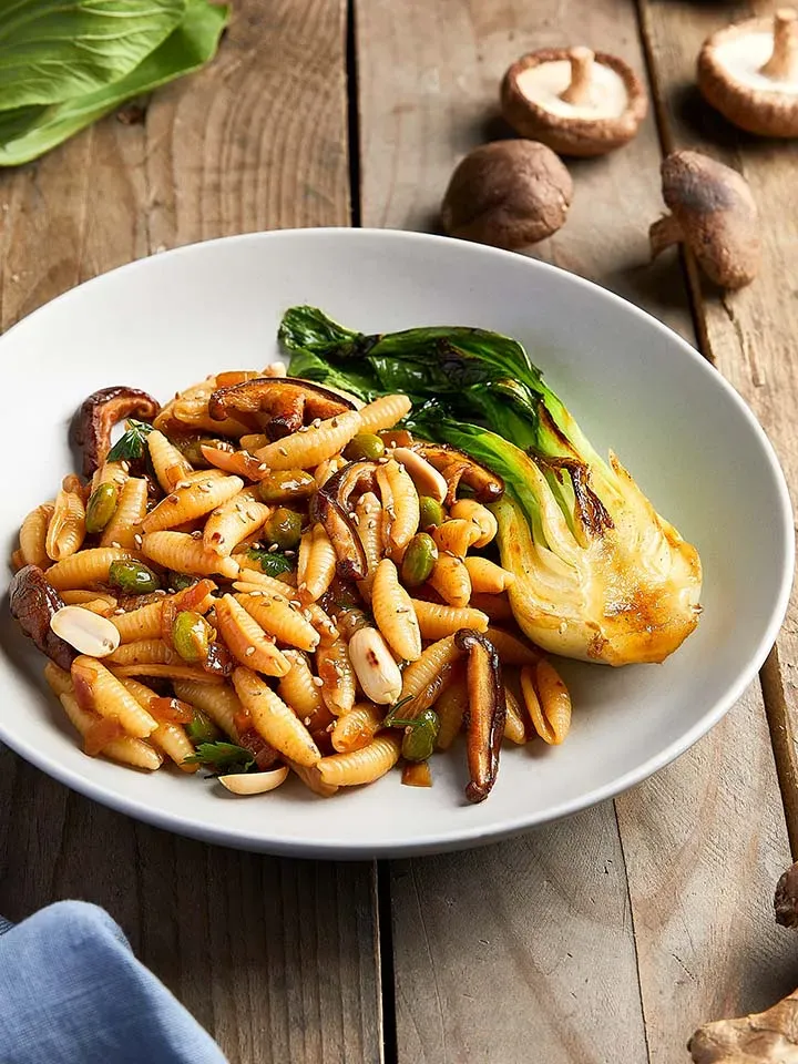 Asia-Pfanne mit Erdnusssauce und Gnocchi sardi, Pilzen und Pak Choi auf einem Teller auf Holztisch