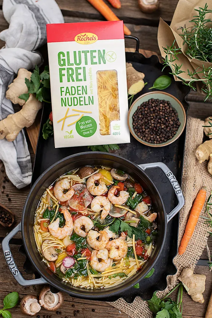 Asiatische Nudelsuppe mit Garnelen und glutenfreien Fadennudeln im Topf auf Holzuntergrund
