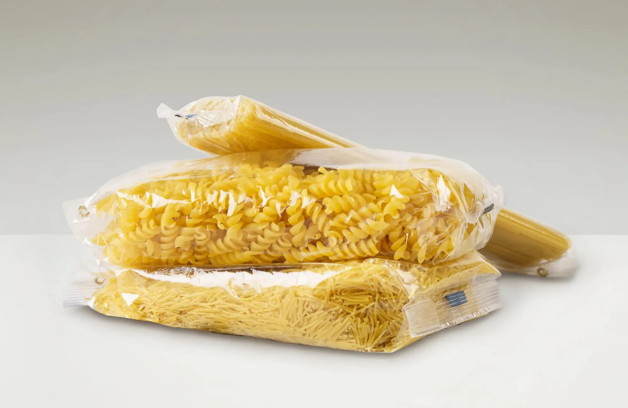 Vier verschiedene ungekochte Nudelsorten in Plastikverpackungen auf weißem Untergrund