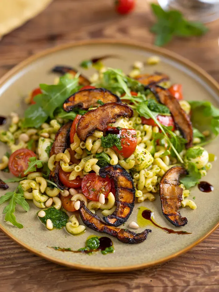 Portobello-Bacon aus Pilzen: Teller mit Nudelsalat, gegrillten Pilzen, Kirschtomaten und Rucola