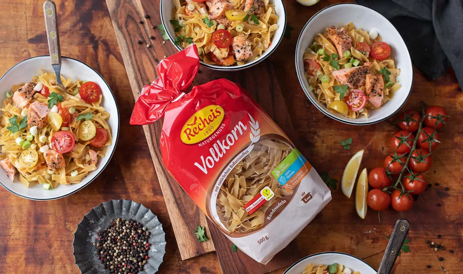 Vollkorn-Bandnudeln mit Lachs und Tomaten in Schalen auf Holztisch neben Nudeltüte