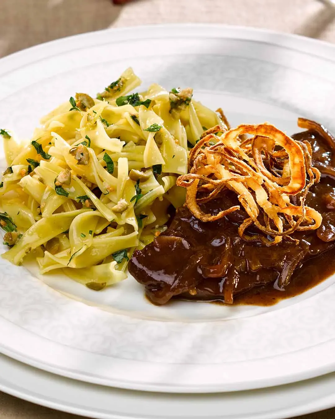 Bandnudeln mit Feinspitz-Rostbraten und Röstzwiebeln auf einem Teller