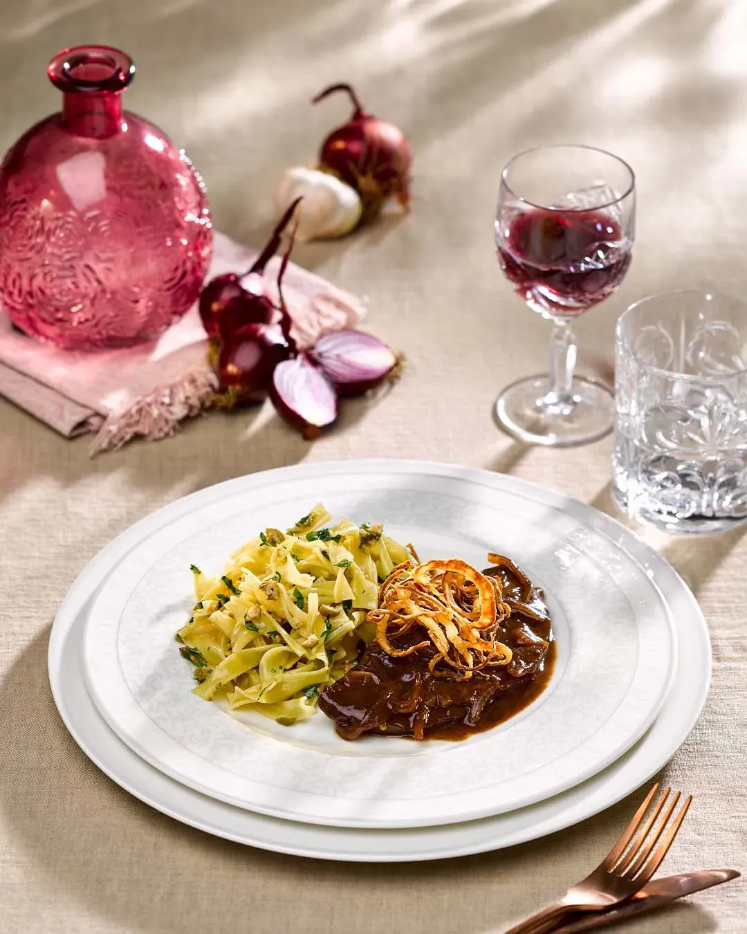 Bandnudeln mit Feinspitz-Rostbraten in Sauce und gebratenen Zwiebeln auf einem Tisch mit Rotwein
