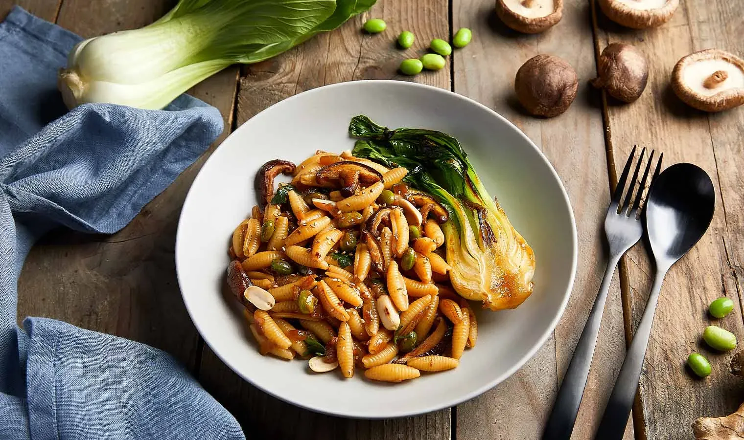 Bio-Gnocchi sardi als Asia-Pfanne mit gebratenem Pak Choi und Pilzen auf einem Teller auf Holztisch mit Besteck