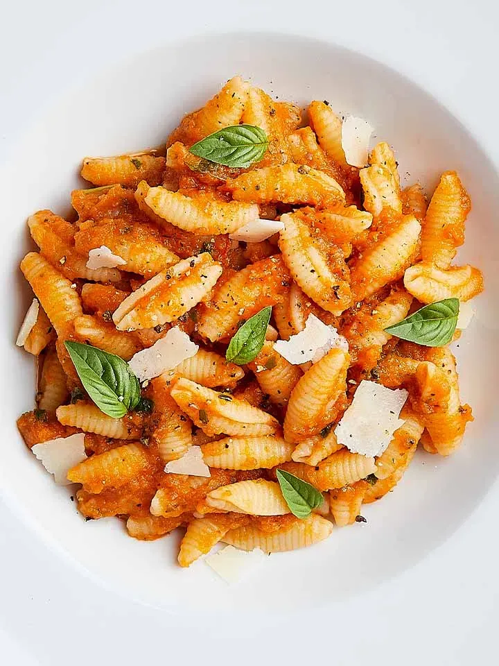 Bio-Gnocchi sardi in Tomatensauce mit Basilikum und Parmesanspänen auf einem Teller, Gemeinschaftsverpflegung