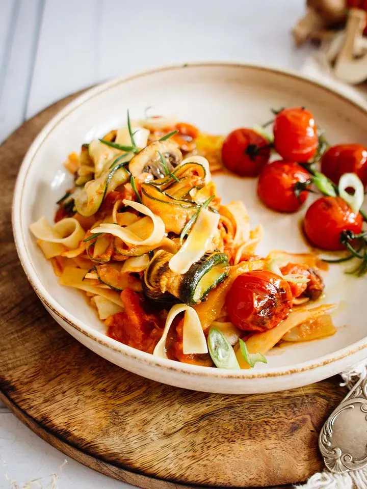 Blitz-Ratatouille mit Vollkorn-Bandnudeln und gerösteten Kirschtomaten auf einem Teller auf Holzbrett