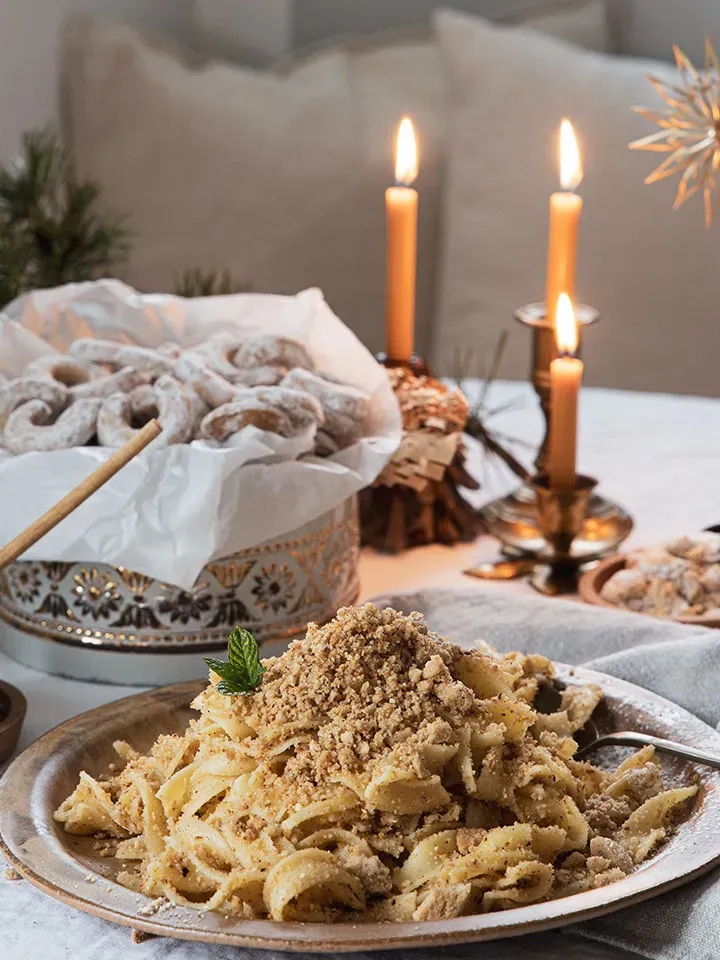 Bröselnudeln mit Schokosauce und Streuseln auf einem Teller vor Kerzen und Weihnachtsgebäck