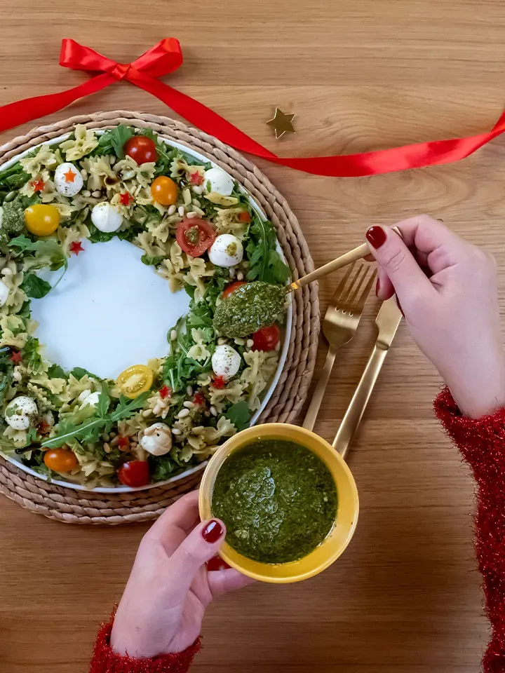 Weihnachtlicher Caprese-Nudelsalat in Kranzform mit grünem Pesto und rotem Band