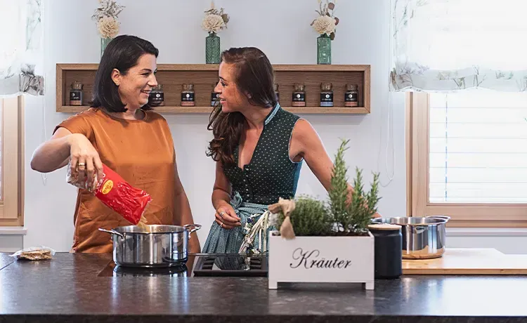 Caroline Pock und Cooking Catrin kochen gemeinsam in der Küche, eine gibt Nudeln aus einer Recheis Packung in den Topf