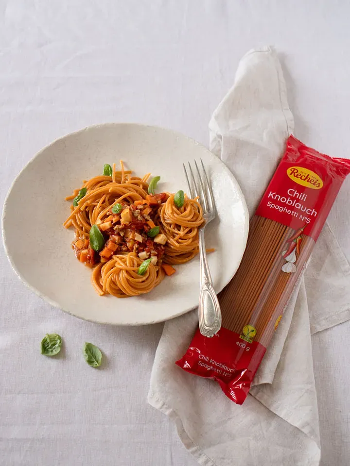 Vegane Chili-Knoblauch-Spaghetti Bolognese auf einem Teller, daneben die Packung auf weißem Tuch