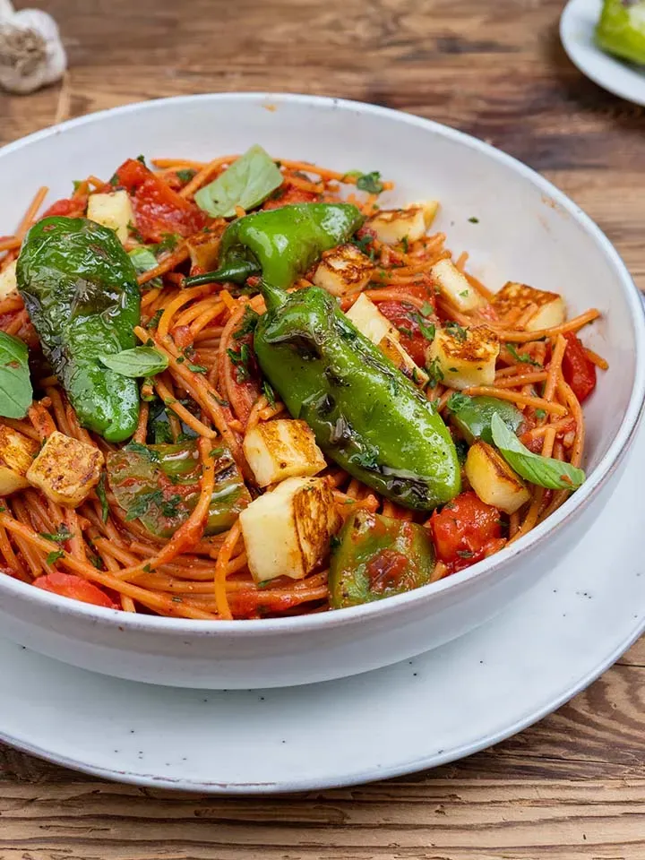 Chili-Knoblauch-Spaghetti mit Bratpaprika, grünen Paprikaschoten und gebratenem Käse auf einem Teller auf Holztisch