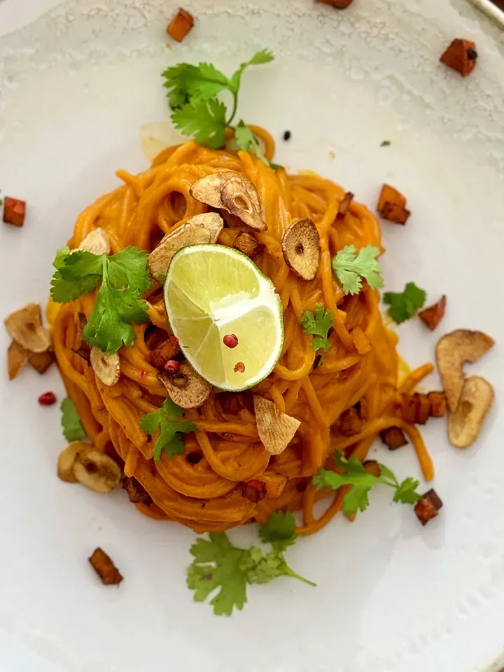 Chili-Knoblauch-Spaghetti mit Kürbis und Gochujang in Nahaufnahme, mit Limettenscheibe, Koriander und Knoblauchchips