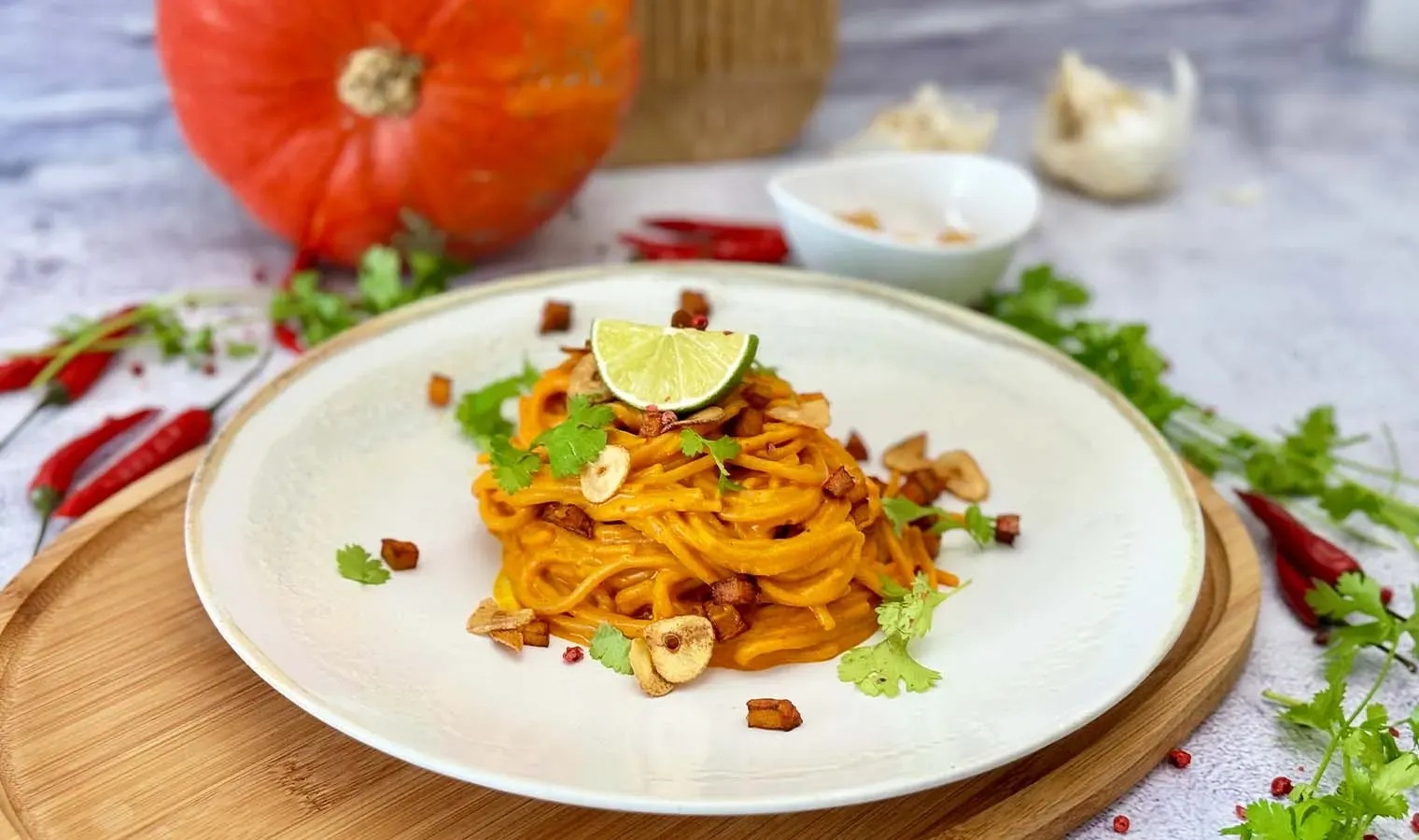 Chili-Knoblauch-Spaghetti mit Kürbis und Gochujang, mit Limettenscheibe und Kräutern garniert, auf Holzbrett