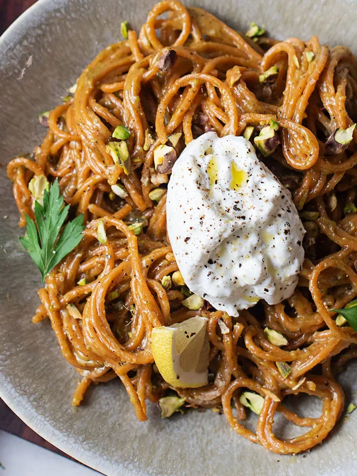 Chili-Knoblauch-Spaghetti mit Pistazien und Burrata in Nahaufnahme, mit Zitronenschnitz und gehackten Nüssen garniert