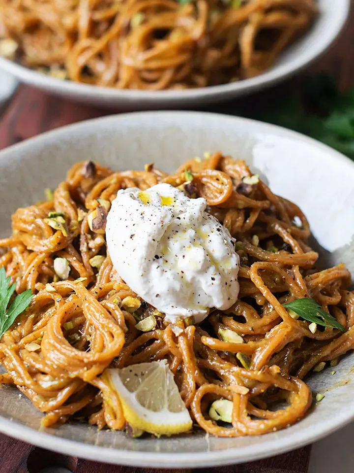 Chili-Knoblauch-Spaghetti mit Pistazien und Burrata, mit Joghurt, Zitronenscheibe und Kräutern garniert, auf einem Teller