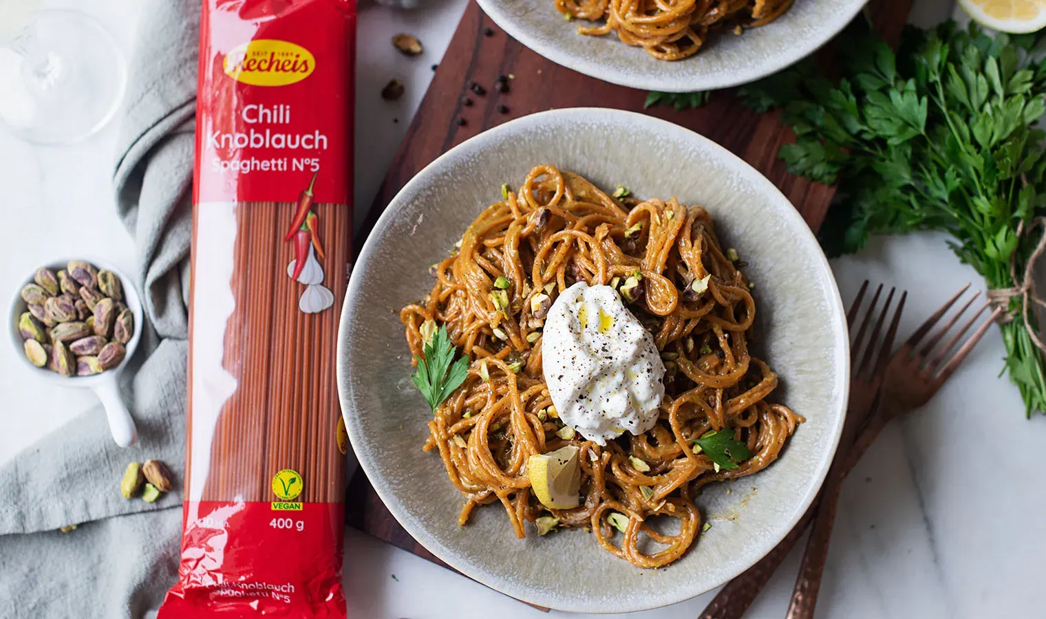 Chili-Knoblauch-Spaghetti mit Pistazien und Burrata von oben, mit Kräutern und einem Klecks Sauce garniert