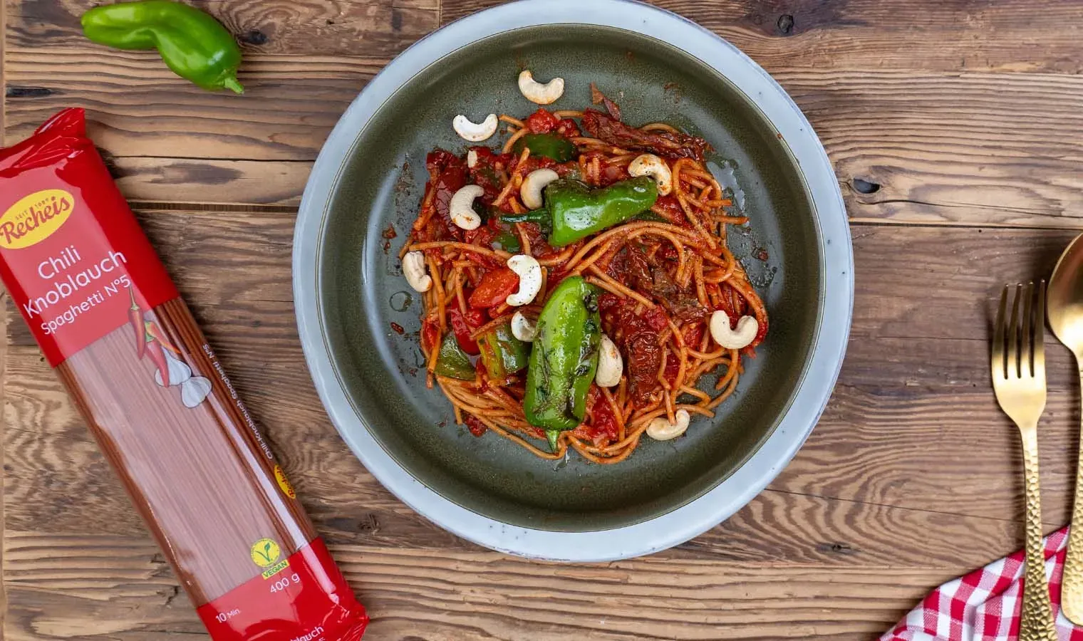 Vegane Chili-Knoblauch-Spaghetti mit Bratpaprika und Cashewnüssen auf einem Teller auf Holzuntergrund