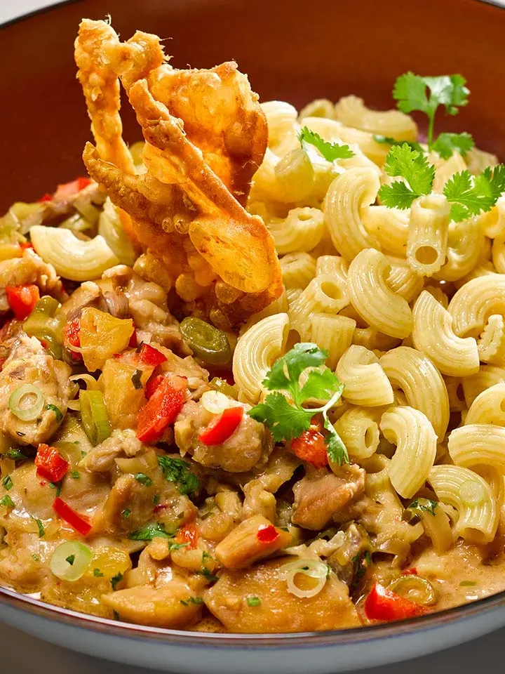 Nahaufnahme: Coconut Hendl, Geschnetzeltes süß-sauer mit Nudeln, Gemüse und Fleisch auf einem Teller