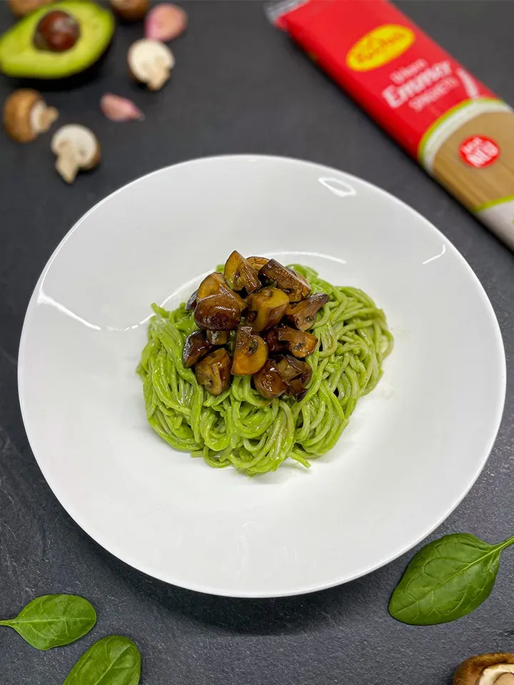 Cremige Avocado-Spaghetti mit gebratenen Champignons auf weißem Teller