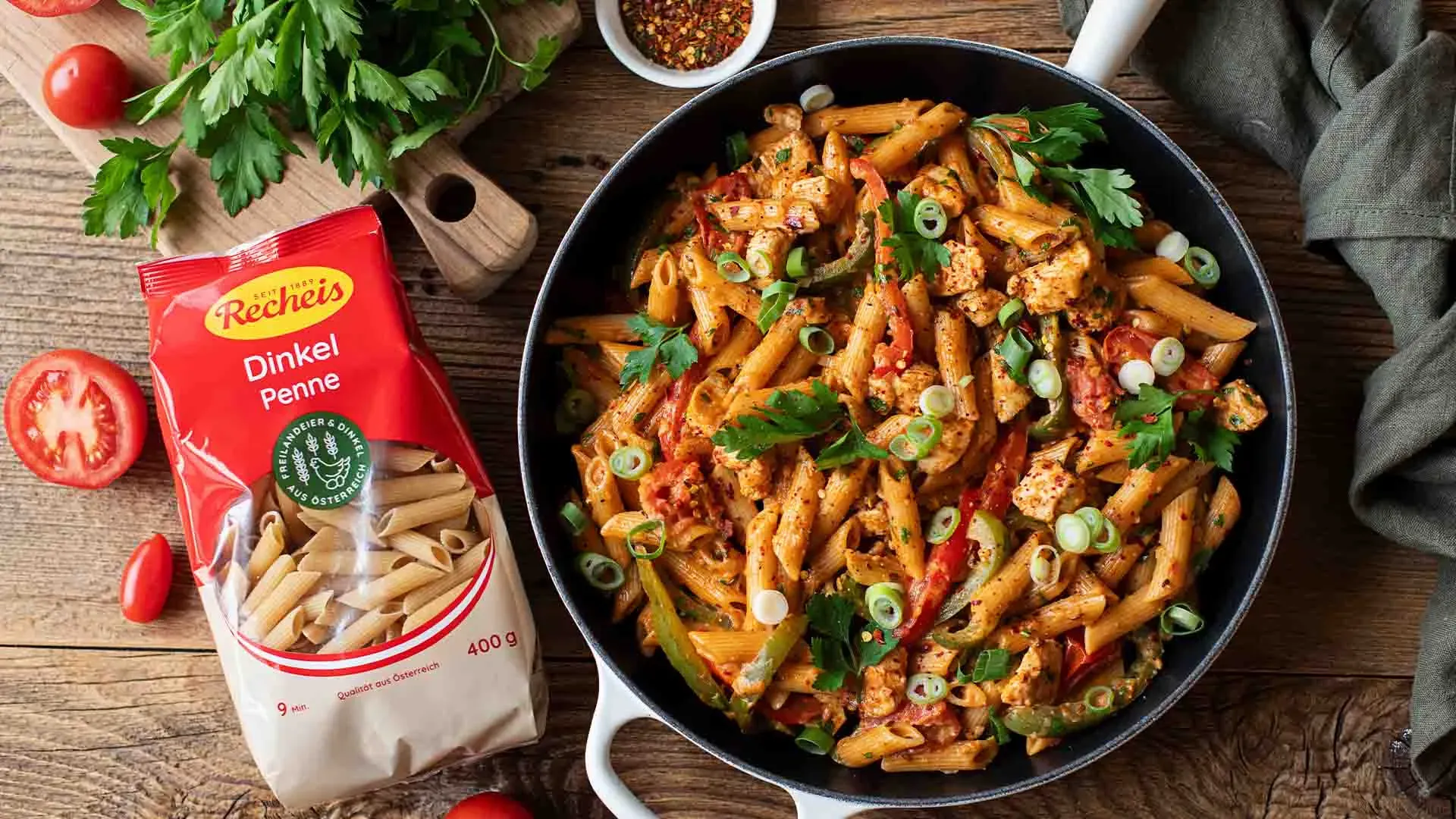 Cremige Cajun-Chicken-Nudelpfanne mit Dinkel-Penne und Gemüse in der Pfanne neben der Packung Dinkel-Penne