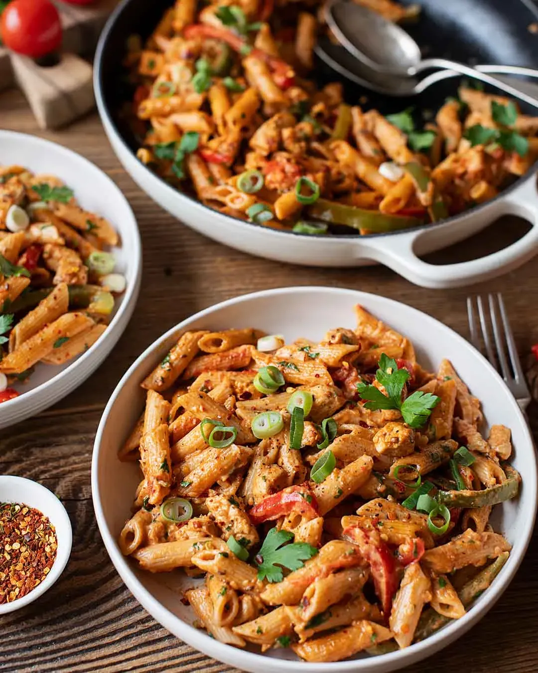 Cremige Cajun-Chicken-Nudelpfanne: Penne mit Gemüse in Tomatensauce auf einem Teller auf Holztisch