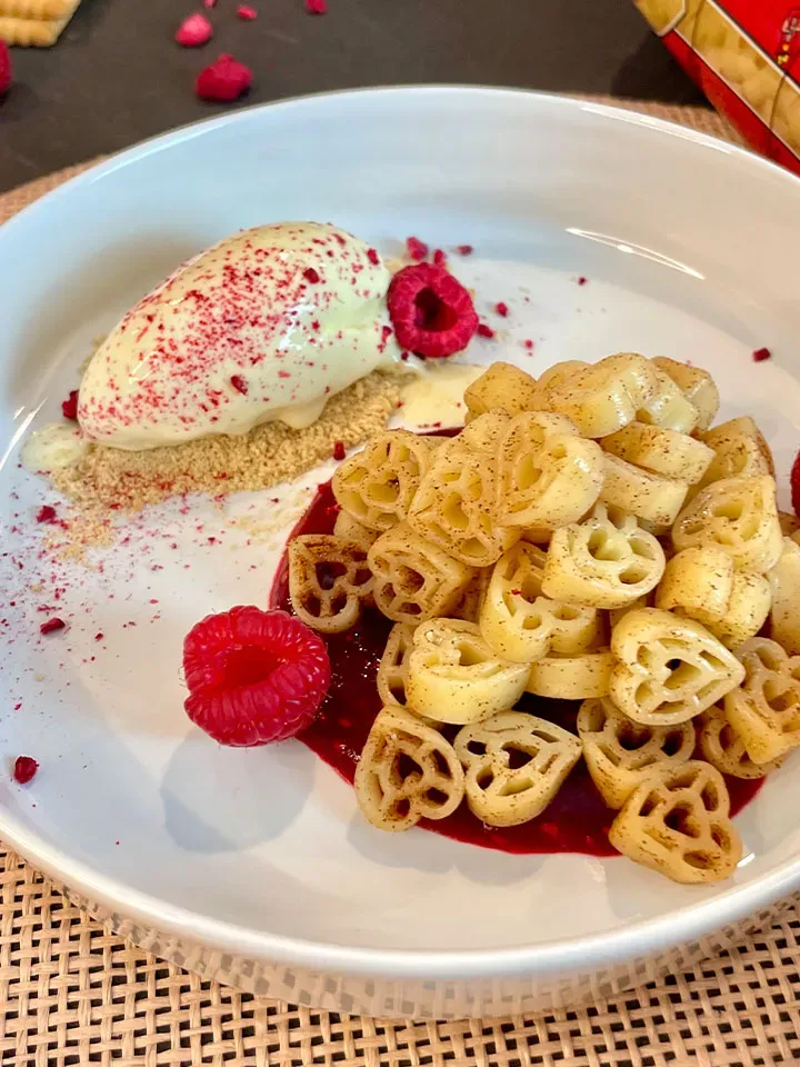 Dessert mit Herznudeln, Himbeersauce und Vanilleeis auf weißem Teller