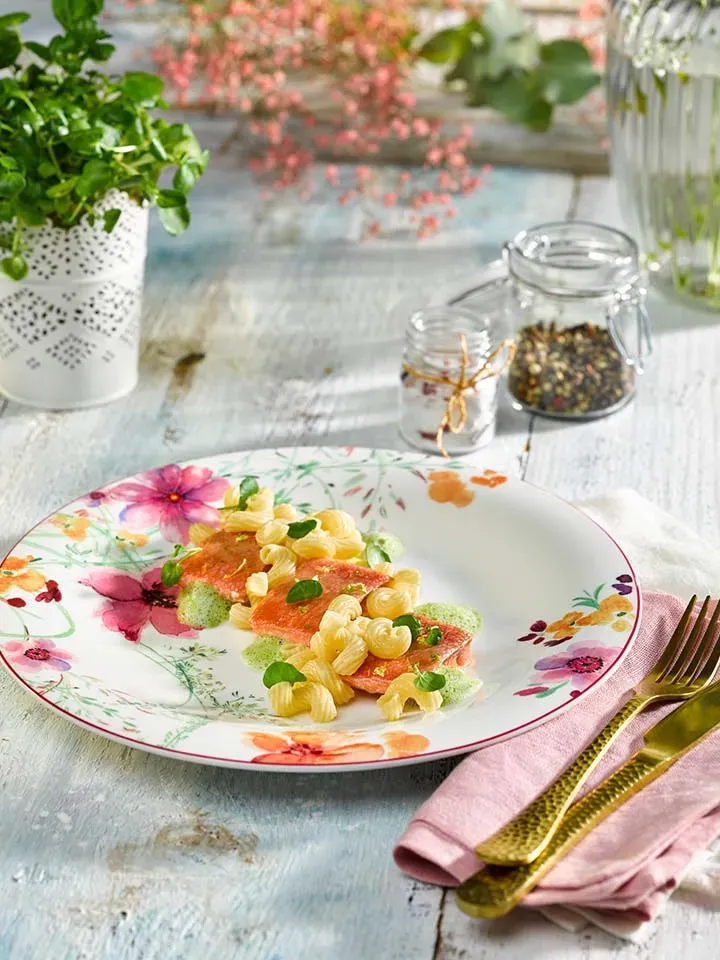 Dinkel-Hörnle mit Goldforelle und grüner Sauce auf einem Blumenmuster-Teller mit Besteck und Pflanzen
