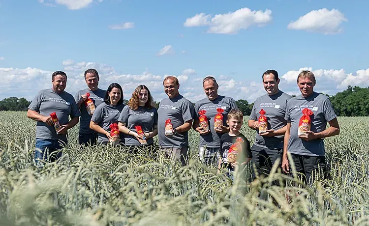 Gruppe von Dinkelbäuerinnen und -bauern in grauen T-Shirts mit Recheis Nudelpackungen in einem Dinkelfeld