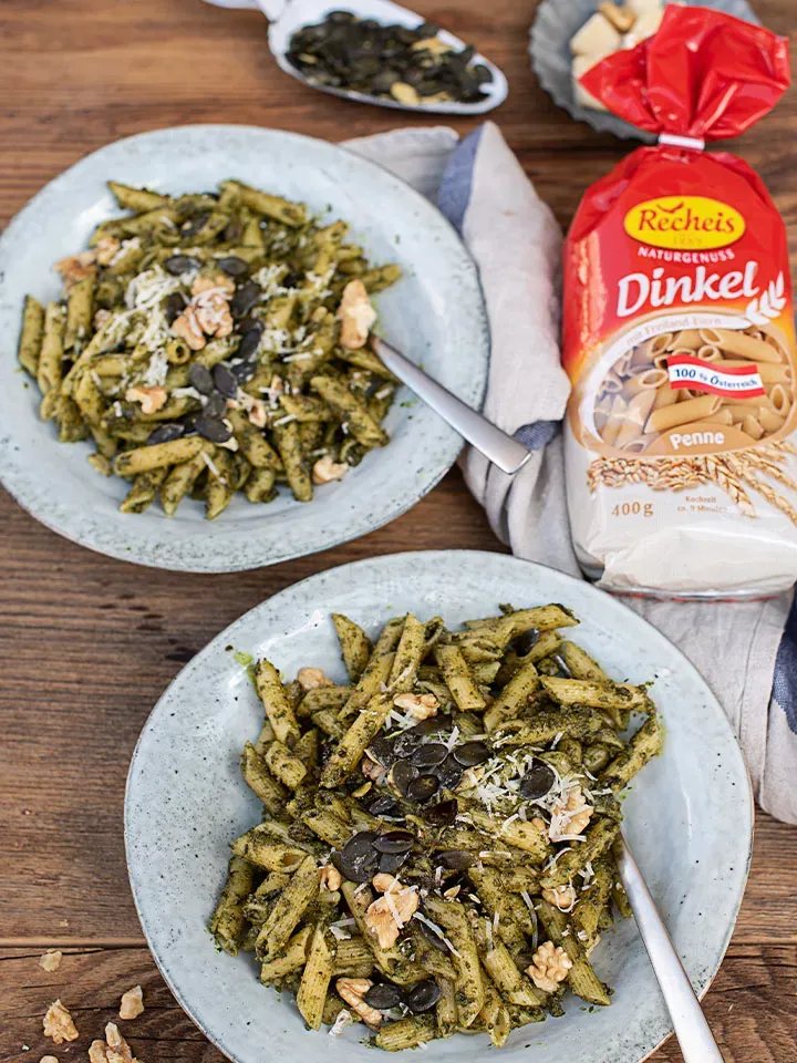 Dinkelpenne mit Bärlauch-Kürbiskernpesto, mit Nüssen und Kernen garniert, auf zwei Tellern