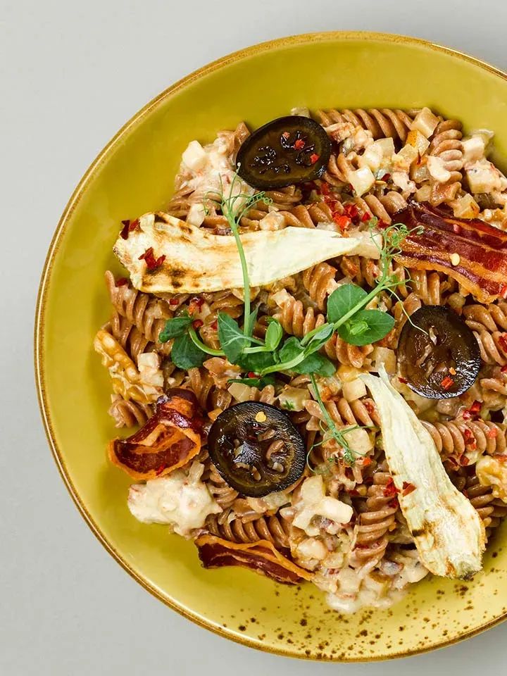 Dralli-Carbonara mit Buddhas Hand, Fusilli mit Gemüsechips und Kräutern auf einem Teller