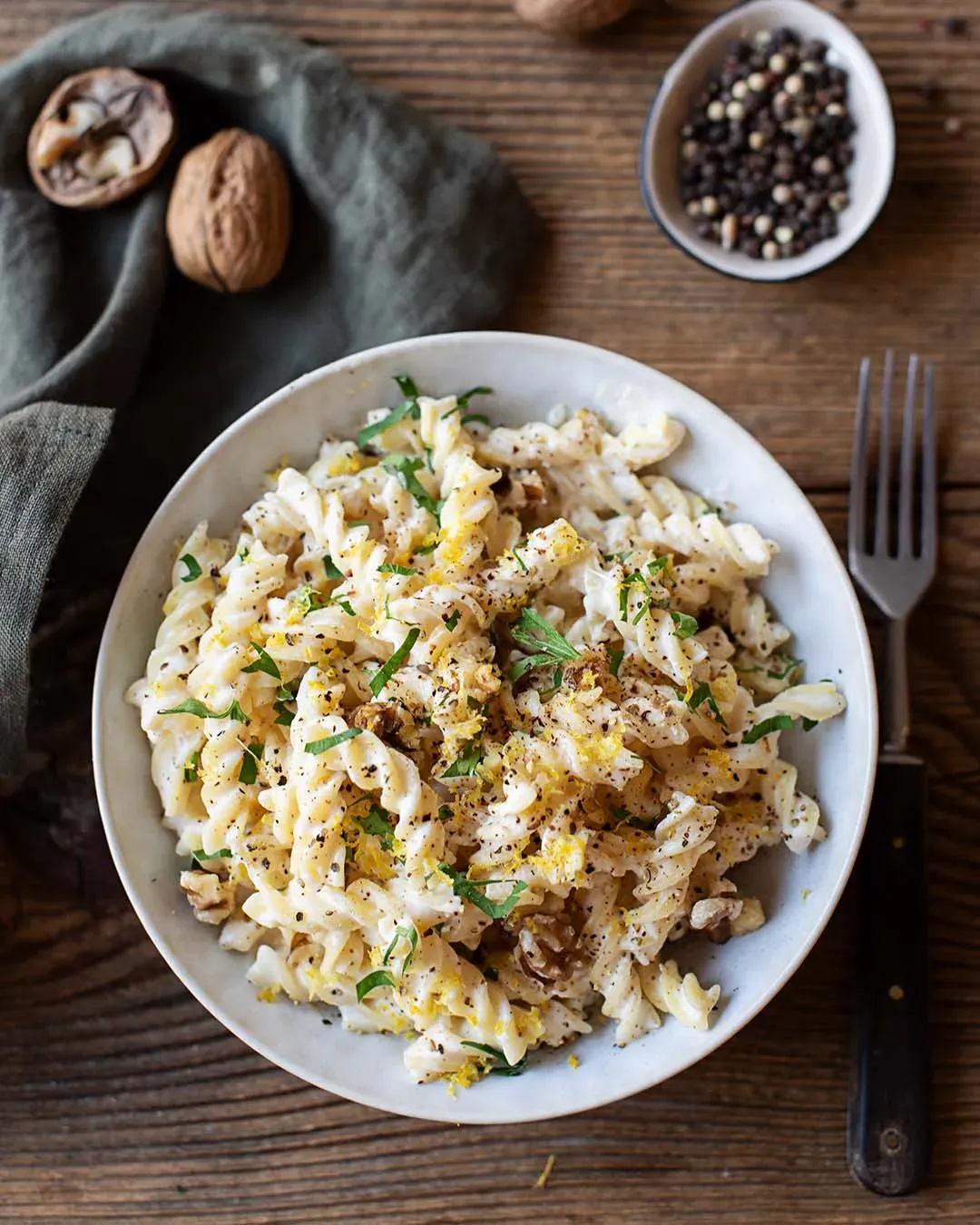 Dralli mit Zitronensauce, cremig, mit Walnüssen und Kräutern auf einem Teller auf Holztisch mit Pfeffer und Gabel