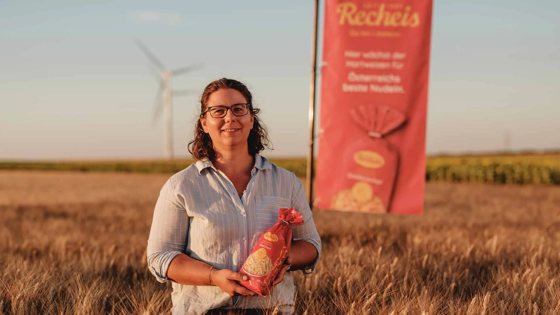 Frau hält Nudeln auf einem Feld mit Windrad und Werbebanner im Hintergrund