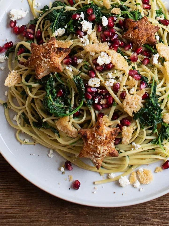 Spaghetti mit einfacher Spinatsauce und Granatapfelkernen, dazu sternförmige Brotscheiben, auf einem Teller