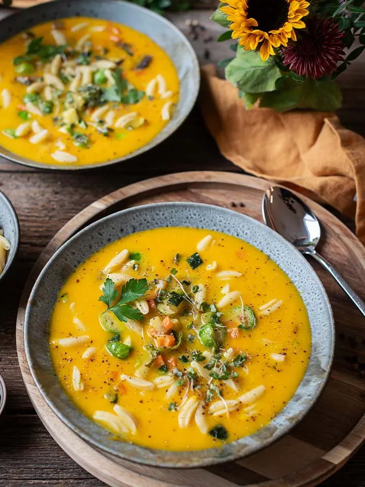 Eintopf mit Nudeln: zwei Schalen gelbe Gemüsesuppe auf Holztisch mit Sonnenblumen