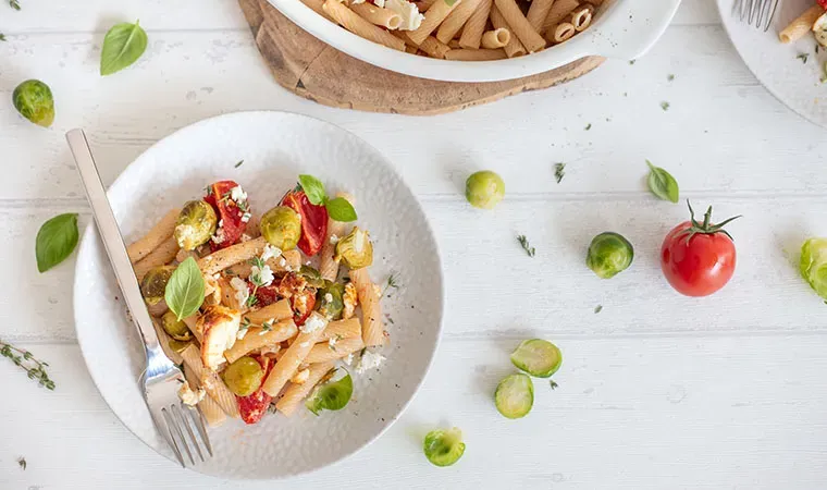 Emmer-Makkaroni mit Kohlsprossen, Feta, Tomaten und Kräutern auf einem Teller auf weißem Tisch