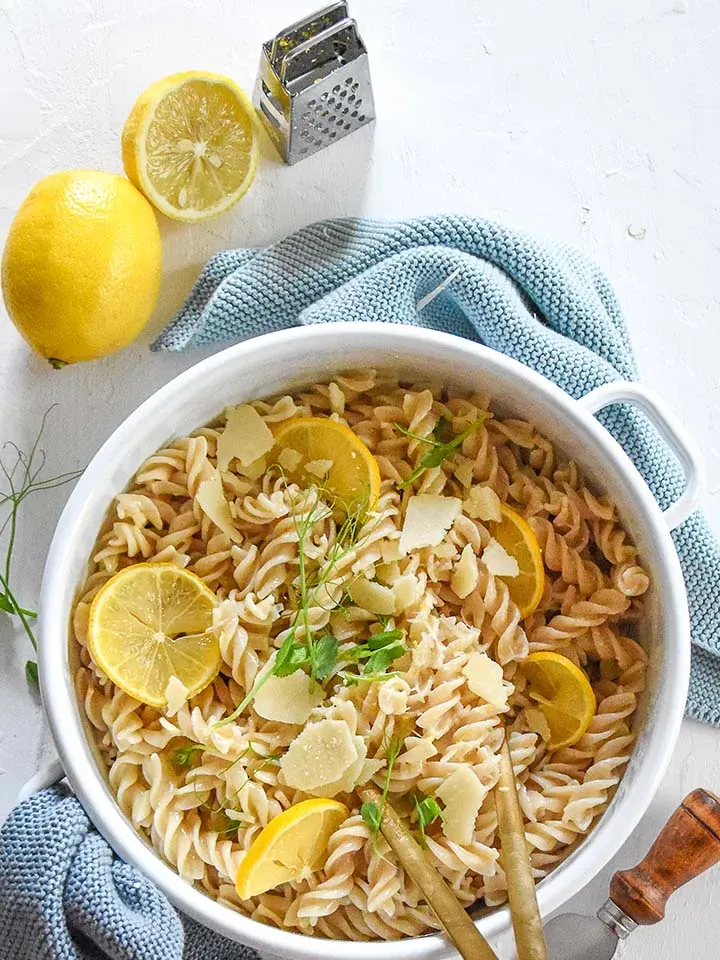 Emmer-Nudeln mit Zitronensauce, Zitronenscheiben und Käse in weißer Schüssel mit Zitronen und Reibe