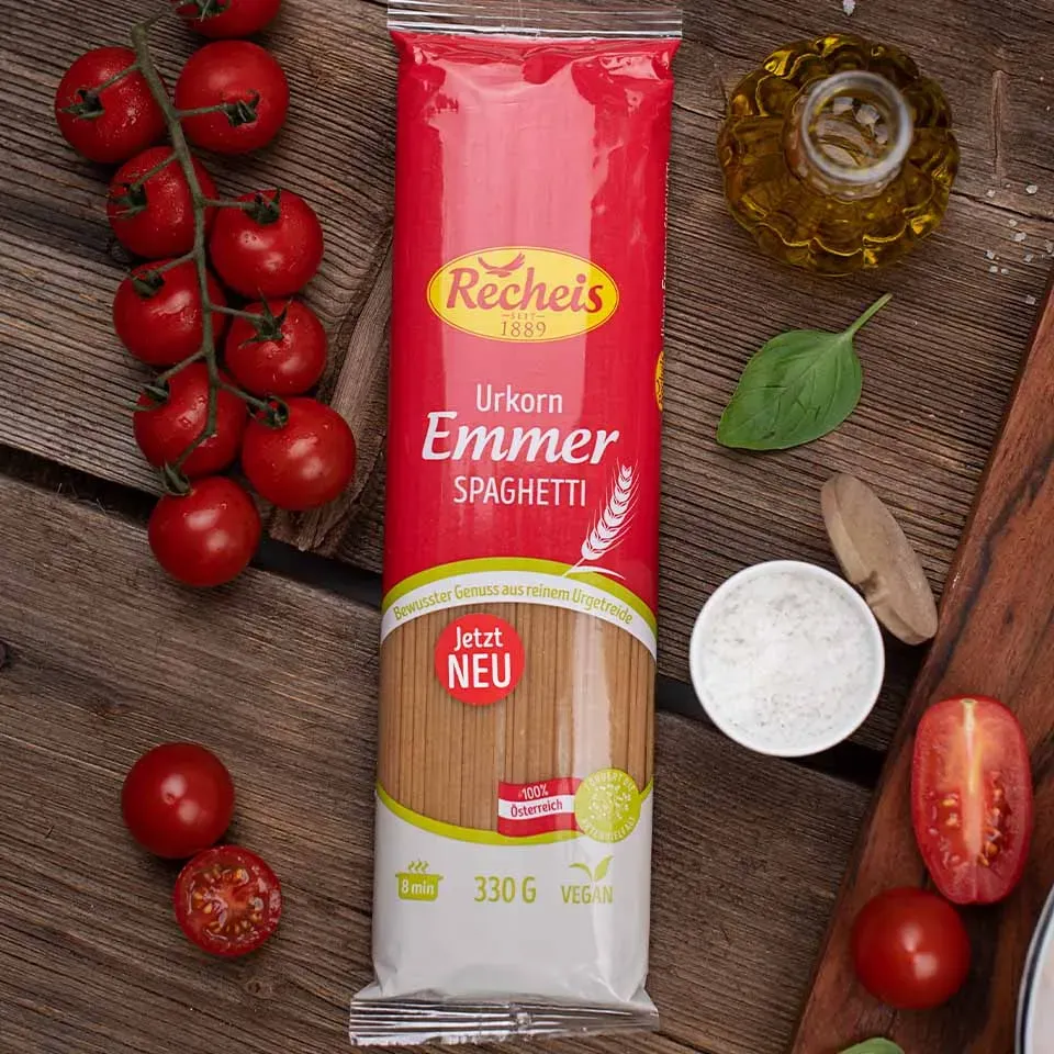 Packung Emmer-Spaghetti mit Tomaten, Basilikum, Salz und Olivenöl auf Holzuntergrund