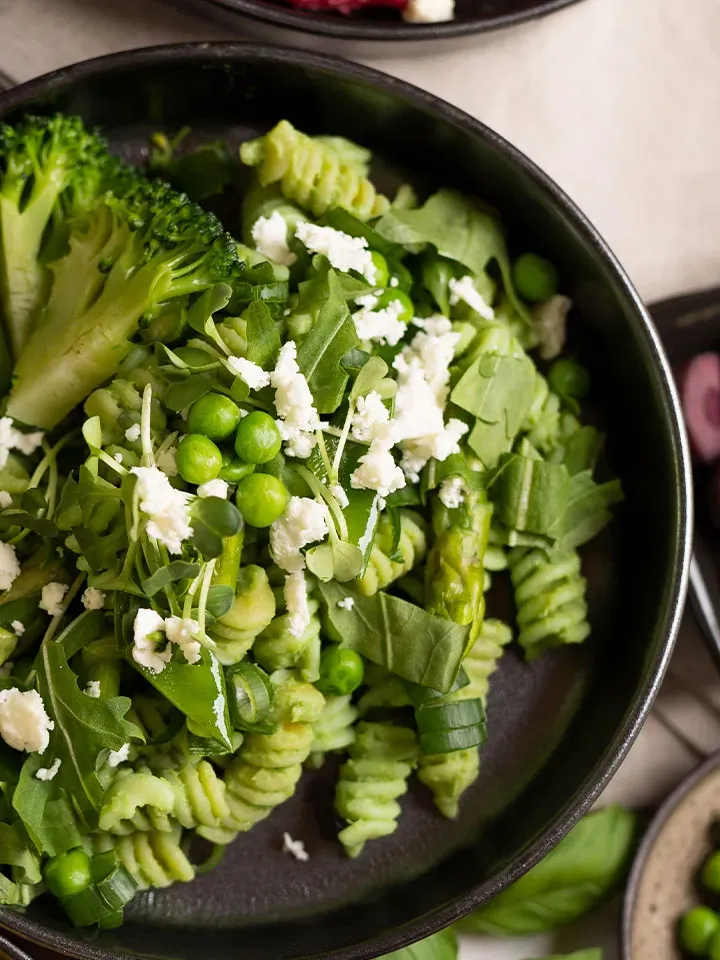 Nudeln mit Erbsencreme, Brokkoli, Rucola und zerbröseltem Käse in schwarzer Schüssel