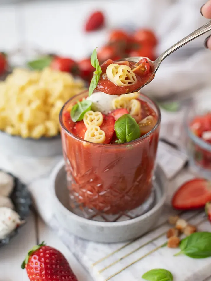 Erdbeer-Tomaten-Gazpacho mit Ziegenfrischkäse und Herzerl Nudeln im Glas, mit Basilikum und Erdbeeren auf einem Löffel