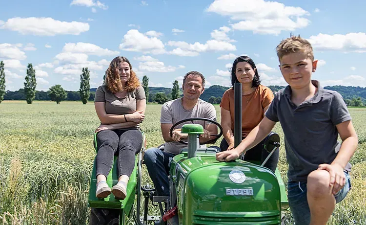 Familie Pock auf und neben einem grünen Oldtimer-Traktor vor einem Dinkelfeld