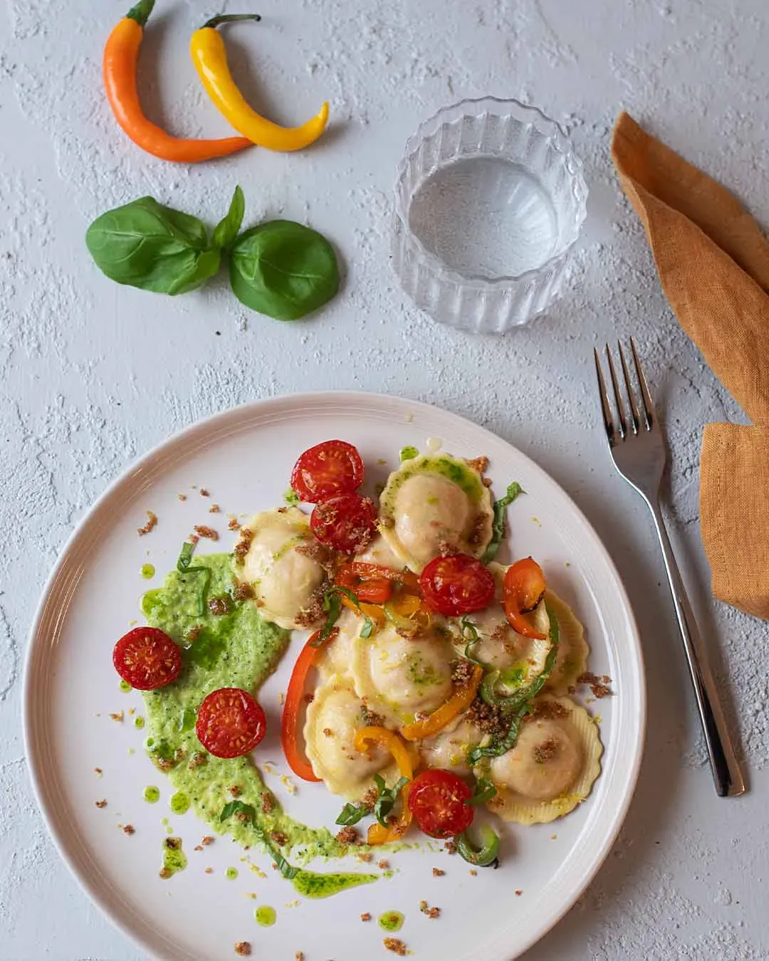 Vegane Fiori Peperonata mit Kirschtomaten, gegrillter Paprika und grünem Pesto auf hellem Untergrund