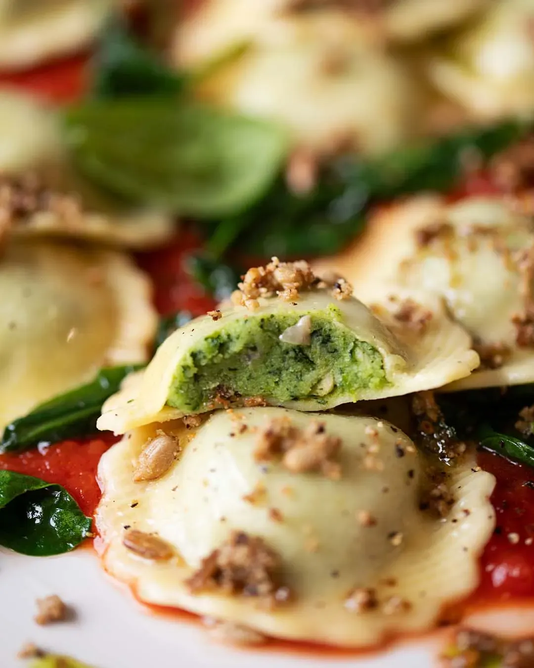 Nahaufnahme: Fiori mit Spinat und Sonnenblumenkernen auf Tomatensauce und Kräutern