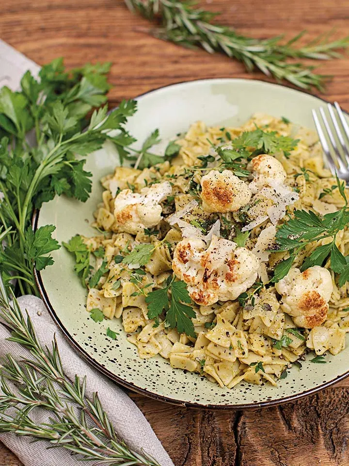 Fleckerl mit Pesto, geröstetem Karfiol und frischen Kräutern auf einem Teller auf Holztisch