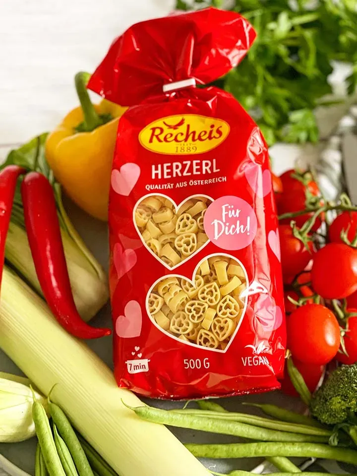 Rote Packung Recheis Herznudeln, umgeben von frischem Frühlingsgemüse